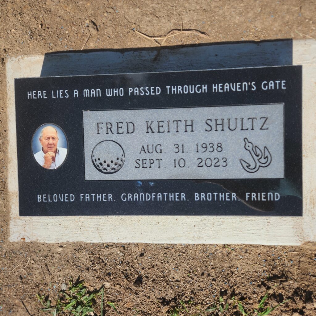 Single flat marker memorial in polished granite with engraved name and dates, lying level with the ground in a landscaped cemetery.