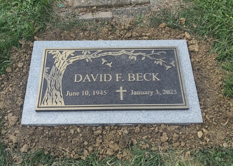 A flat bronze grave marker with personalized name and date inscriptions, securely mounted on a polished granite backer for cemetery use.