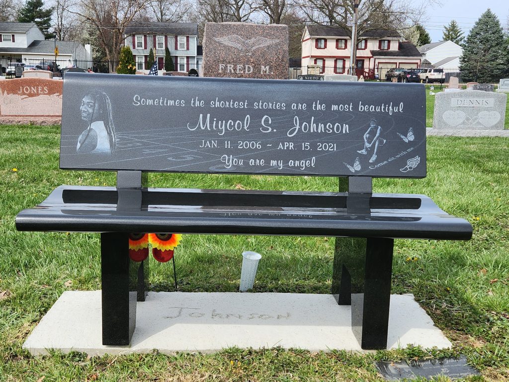A polished black granite garden bench with a full backrest featuring custom laser etching and a photo portrait, representing the premium options in our Garden Bench packages.